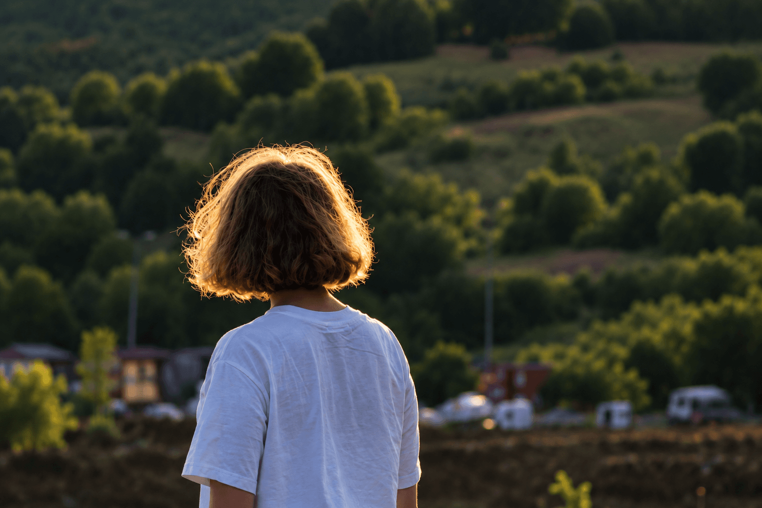 A young person seen from behind, looking out over sunlit hills at golden hour.